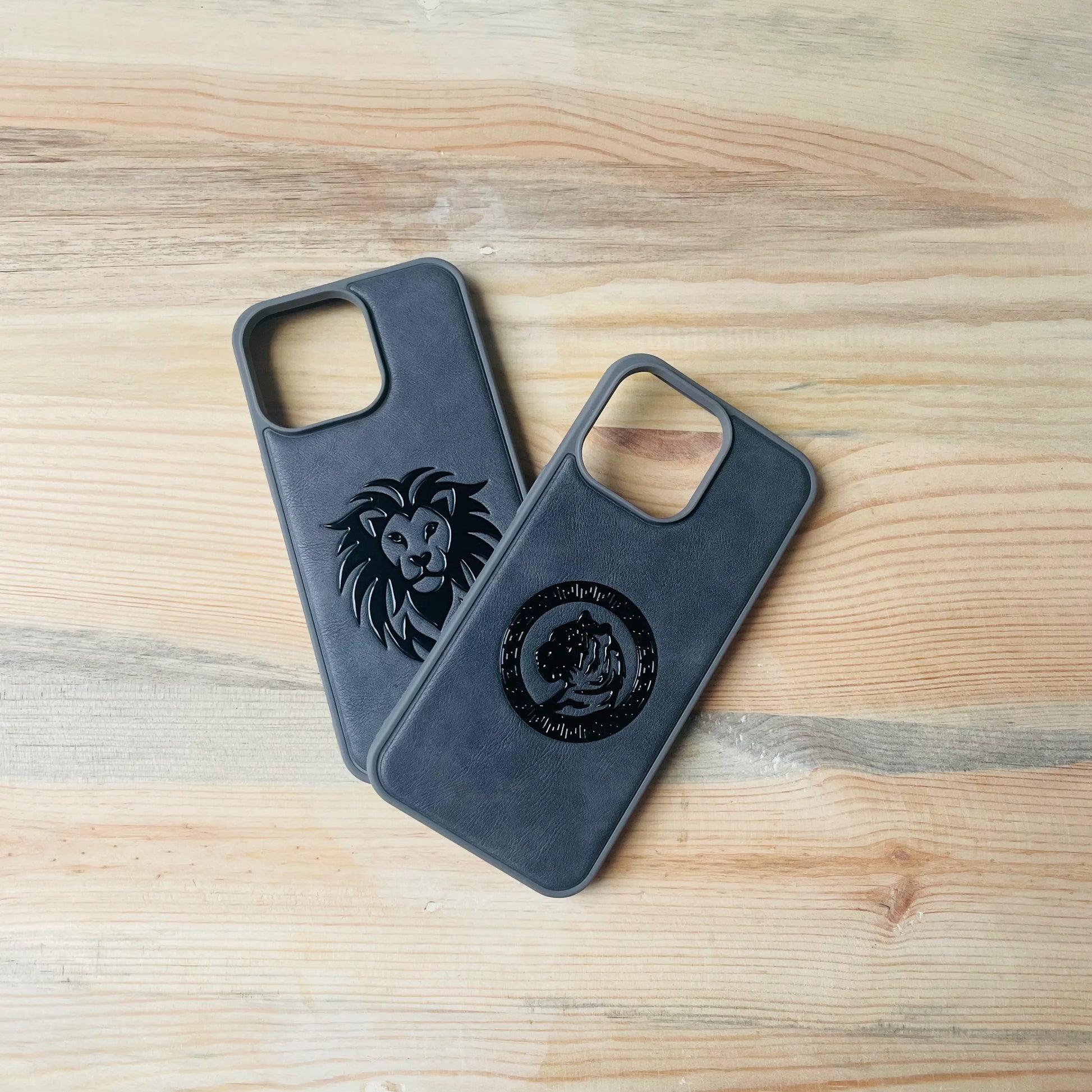 Two dark gray iphone cases with lion emblem designs on a wooden surface