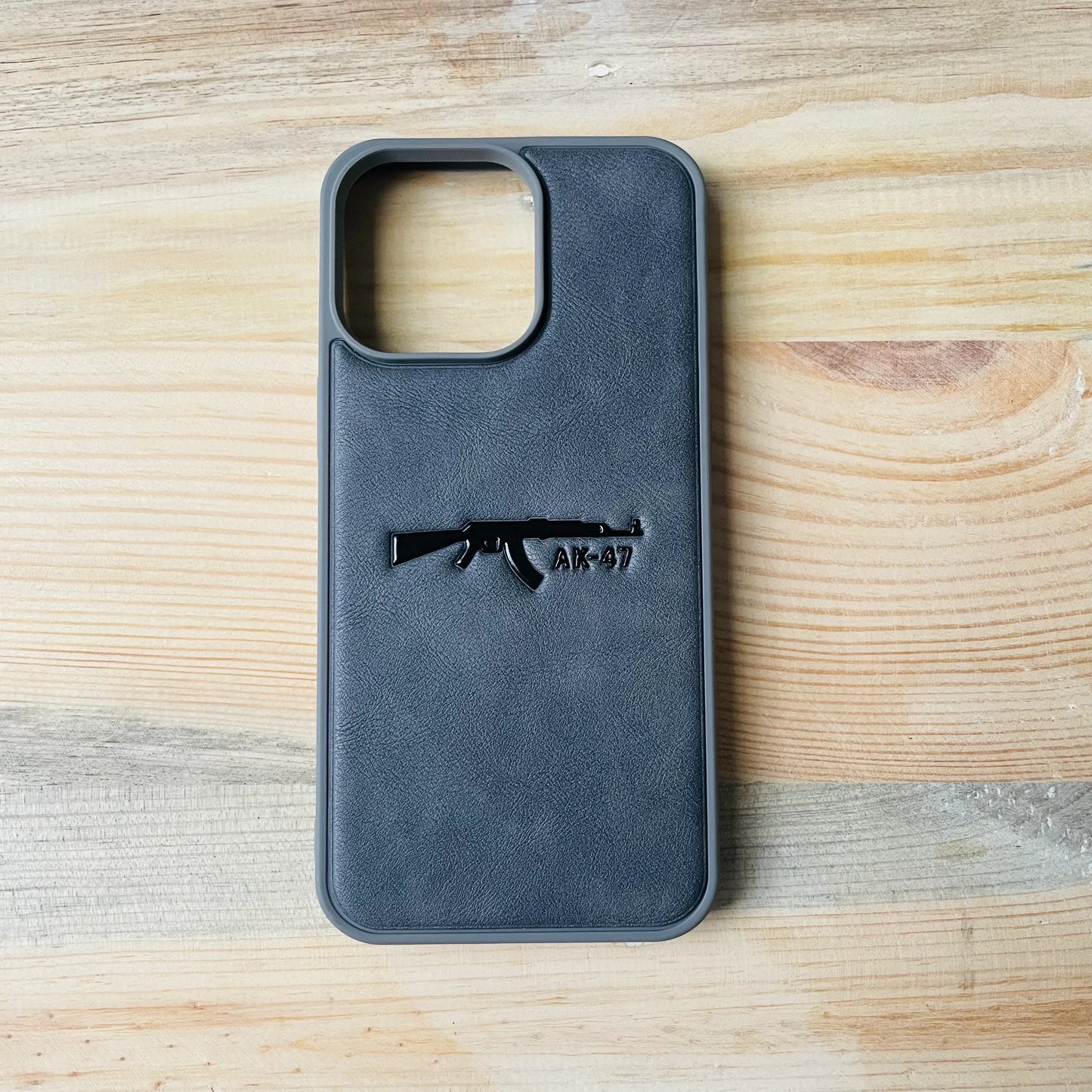 Gray Series | Premium Leather 3D Embossed iPhone case with AK-47 design on a wooden surface